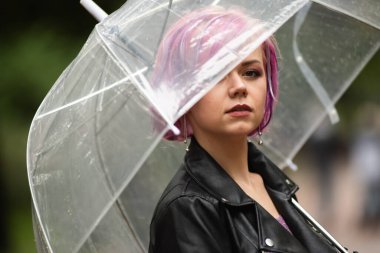 Dışarıda dolaşırken şemsiye tutan neşeli güzel kız. Arkasını dönüp kameraya bakıyor. Gerçek bir zevk ve samimi bir gülümsemeyle..