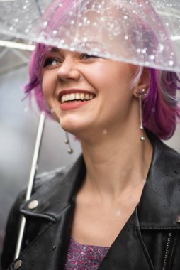 Dışarıda dolaşırken şemsiye tutan neşeli güzel kız. Arkasını dönüp kameraya bakıyor. Gerçek bir zevk ve samimi bir gülümsemeyle..