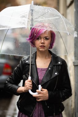 Kurumuş ve korunmuş hissediyorum. Sokakta dururken şemsiye taşıyan ve gülümseyen çekici genç bir kadın.