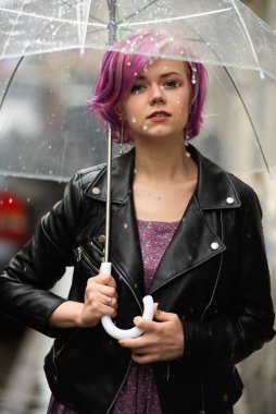 Kurumuş ve korunmuş hissediyorum. Sokakta dururken şemsiye taşıyan ve gülümseyen çekici genç bir kadın.