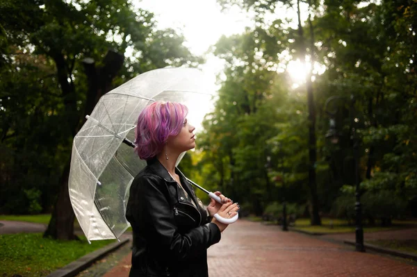 Dışarıda dolaşırken şemsiye tutan neşeli güzel kız. Arkasını dönüp kameraya bakıyor. Gerçek bir zevk ve samimi bir gülümsemeyle..