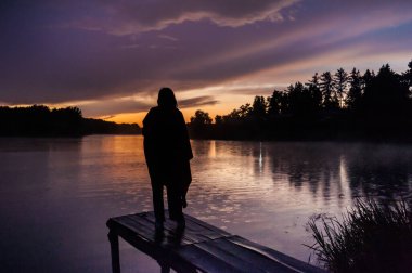 Adam gün batımında iskelede duruyor.