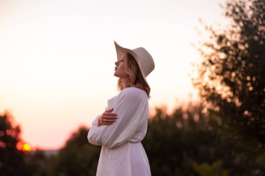 beautiful girl in a white dress and hat in a lavender field at sunset