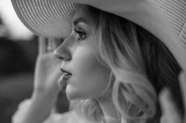 beautiful blonde girl in a hat and a white shirt on a background of a summer day