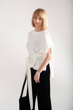 Siyah elbiseli, uzun saçlı, beyaz gömlekli, gri arka planda güzel bir sarışın kadın.