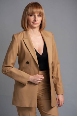 Siyah ceketli ve gri arka planda beyaz gömlekli güzel bir kadın.