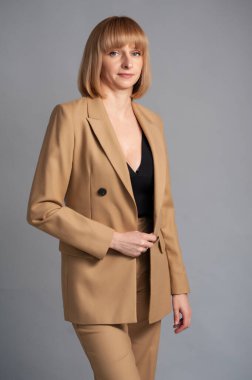 Gri arka planda siyah bir elbise ve bej ceketli güzel bir kadın.