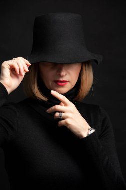 Siyah şapkalı, beyaz gömlekli, siyah arka planda güzel bir kadın.