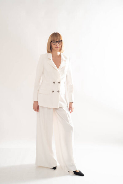 portrait of a beautiful young woman in a white suit and glasses on a gray background