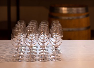 Şarap tatmaya hazır beyaz bir masa örtüsü, matris, arka planda şarap fıçısı olan bir masada sıralanmış kristal şarap kadehleri.