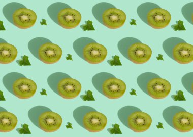 Fruit pattern on a pastel green background. Creative layout of kiwi and leaves, summer concept.