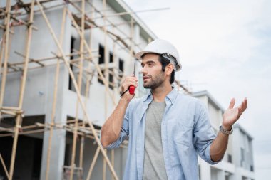 İnşaat alanında duran genç erkek mühendisler taşınabilir telsizle konuşuyorlar ve çeşitli fonksiyonları kontrol ediyorlar..