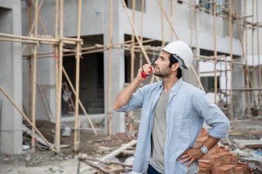 İnşaat alanında duran genç erkek mühendisler taşınabilir telsizle konuşuyorlar ve çeşitli fonksiyonları kontrol ediyorlar..