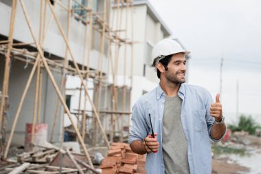 İnşaat alanında duran genç erkek mühendisler taşınabilir telsizle konuşuyorlar ve çeşitli fonksiyonları kontrol ediyorlar..
