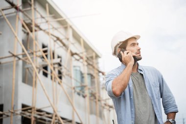İnşaat alanında duran genç erkek mühendisler taşınabilir telsizle konuşuyorlar ve çeşitli fonksiyonları kontrol ediyorlar..