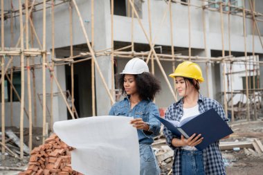 Mühendis ve kadın ustabaşı çeşitli işlevleri kontrol etmek için inşaat alanında duruyorlar..