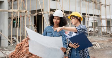 Mühendis ve kadın ustabaşı çeşitli işlevleri kontrol etmek için inşaat alanında duruyorlar..