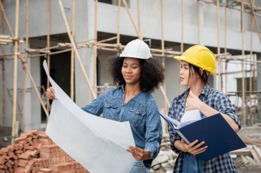 Mühendis ve kadın ustabaşı çeşitli işlevleri kontrol etmek için inşaat alanında duruyorlar..