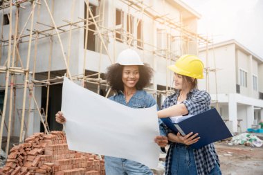 Mühendis ve kadın ustabaşı çeşitli işlevleri kontrol etmek için inşaat alanında duruyorlar..