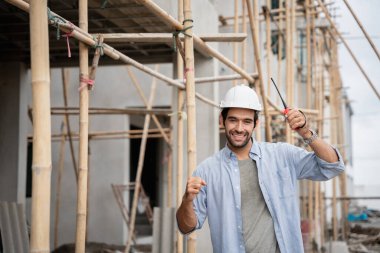 İnşaat alanında duran genç erkek mühendisler taşınabilir telsizle konuşuyorlar ve çeşitli fonksiyonları kontrol ediyorlar..