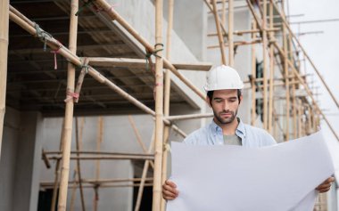 İnşaat alanında duran genç erkek mühendisler çeşitli fonksiyonları kontrol ediyorlar..