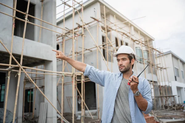 İnşaat alanında duran genç erkek mühendisler taşınabilir telsizle konuşuyorlar ve çeşitli fonksiyonları kontrol ediyorlar..