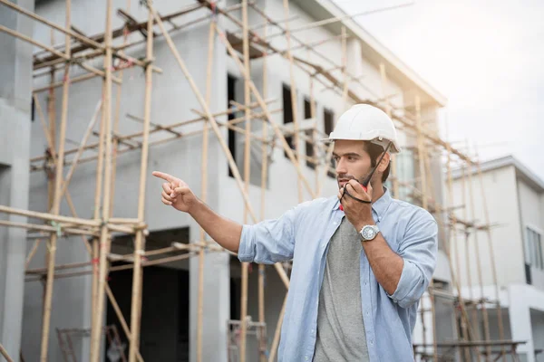 İnşaat alanında duran genç erkek mühendisler taşınabilir telsizle konuşuyorlar ve çeşitli fonksiyonları kontrol ediyorlar..