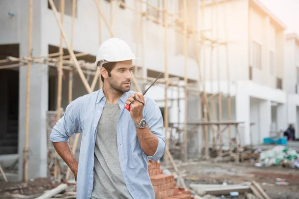 İnşaat alanında duran genç erkek mühendisler taşınabilir telsizle konuşuyorlar ve çeşitli fonksiyonları kontrol ediyorlar..