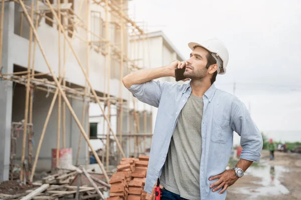 İnşaat alanında duran genç erkek mühendisler taşınabilir telsizle konuşuyorlar ve çeşitli fonksiyonları kontrol ediyorlar..