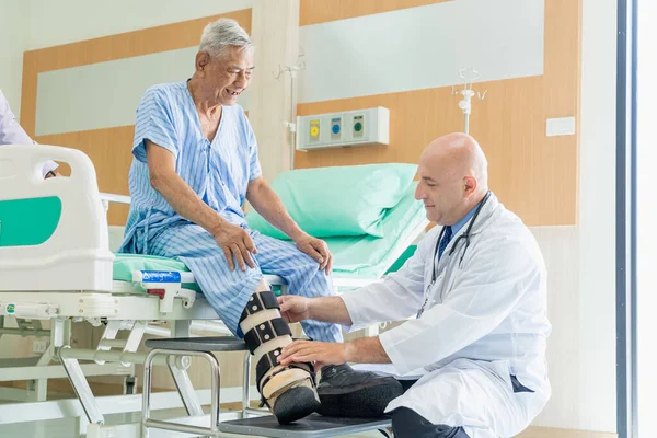 Bir erkek doktor hastanede diz sorunu olan bir hastanın kafasını muayene eder..