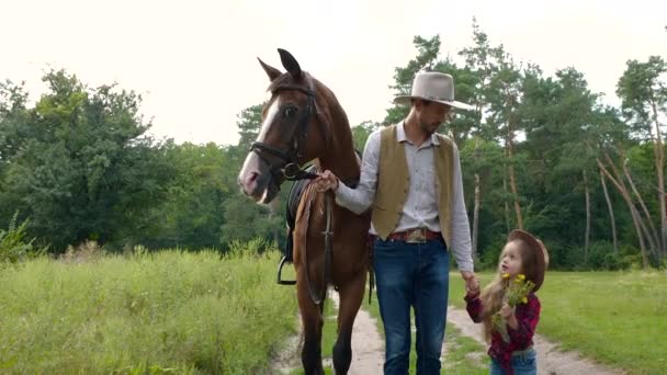 Cowboy with his daughter walking with a horse on a forest road — Stock Video