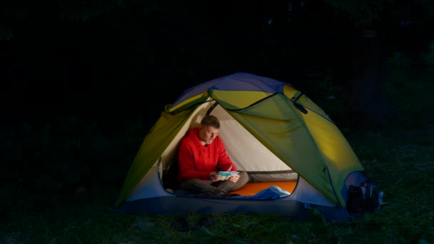 Человек пролистывает записную книжку в палатке в ночном лесу — стоковое видео