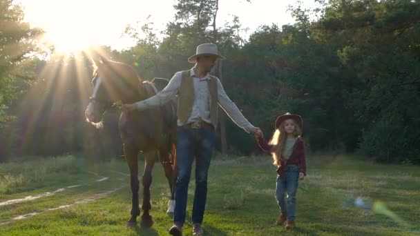 Un vaquero con un caballo y su hermosa hija están caminando en el pasto — Vídeo de stock