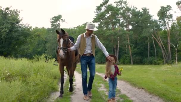 Cowboy met zijn dochter wandelen met een paard op een bosweg — Stockvideo