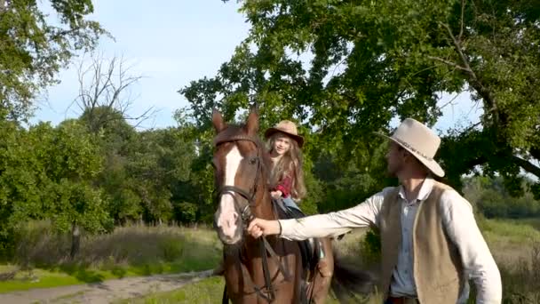 Um jovem cowboy está liderando um cavalo no qual sua filha está sentada — Vídeo de Stock