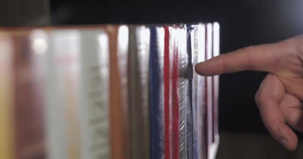 Una mano de hombre está buscando el libro correcto entre una colección de volúmenes — Vídeo de stock