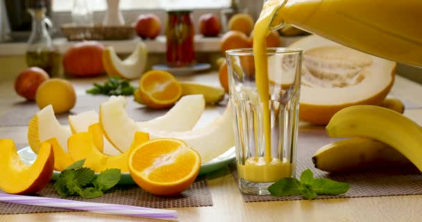 Melón plátano naranja Smoothie se vierte en un vaso sobre el fondo de frutas frescas — Vídeos de Stock