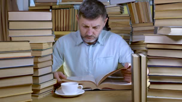 Un uomo barbuto legge un libro in biblioteca — Video Stock