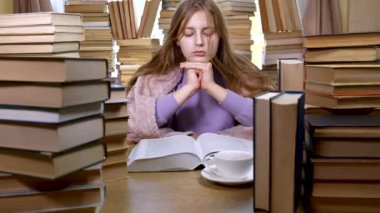 Bir kız kütüphanede kitap okuyor.