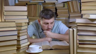 Sakallı bir adam kütüphanede kitap okuyor.