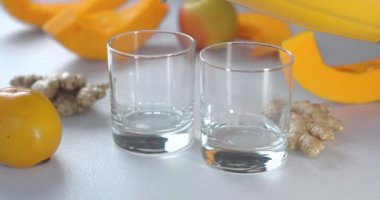 Balkabağı ve zencefilli içecekler bardaklara doldurulur. Taze sebze ve meyvelerin arka planına karşı..