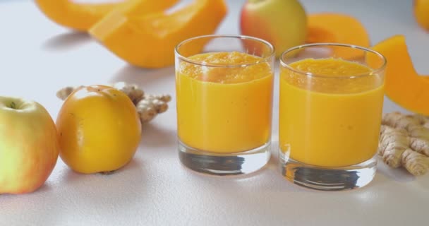 Pumpa och ingefära smoothie hälls i glas mot bakgrund av färska grönsaker och frukter. — Stockvideo