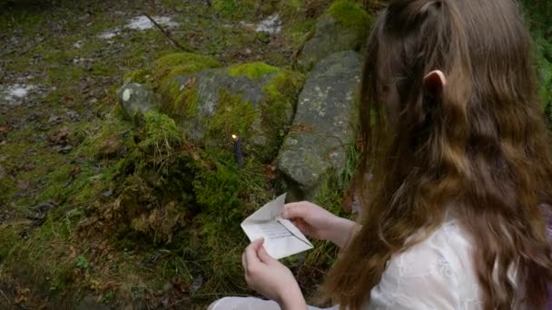 Ельф дівчина в білій сукні відкриває конверт з літерами в лісі — стокове відео