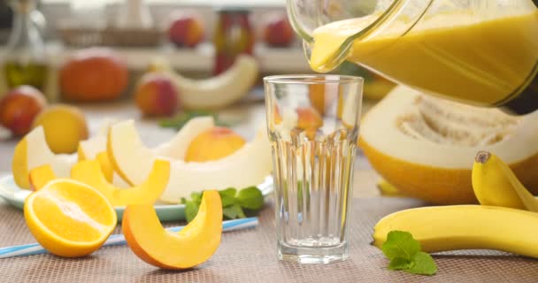 メロンバナナオレンジ新鮮な果物の背景にガラスにスムージーを注ぎます — ストック動画