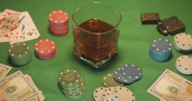 Fişler, kartlar, bir bardak viski ve para yeşil oyun masasında.