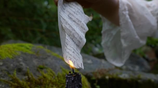 Эльфийская девушка в белом платье сжигает письмо в лесу — стоковое видео