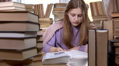 Bir kız kütüphanede kitap okuyor.