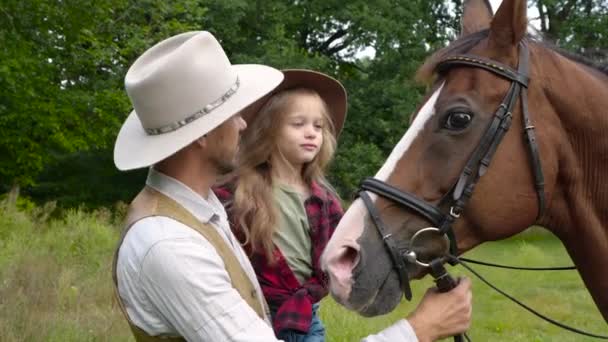 Ковбой и его дочь гладят лошадь — стоковое видео