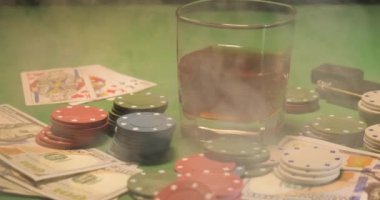 Fişler, kartlar, bir bardak viski ve para yeşil oyun masasında.