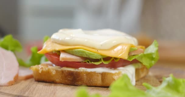 Grande sanduíche apetitoso com presunto, fatias de tomate maduro e pedaços de queijo, alface e molho de maionese — Vídeo de Stock